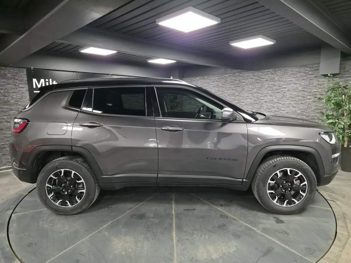 Vue de profil côté gauche d'un Jeep Compass gris métallisé avec toit noir, roues noires et détails Trailhawk.