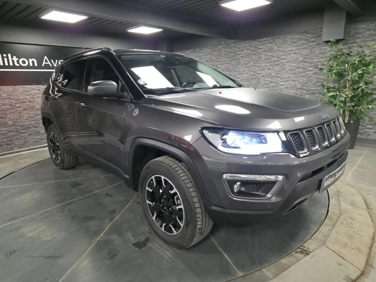 Jeep Compass gris métallisé en 3/4 avant droit avec phares allumés dans un showroom intérieur.
