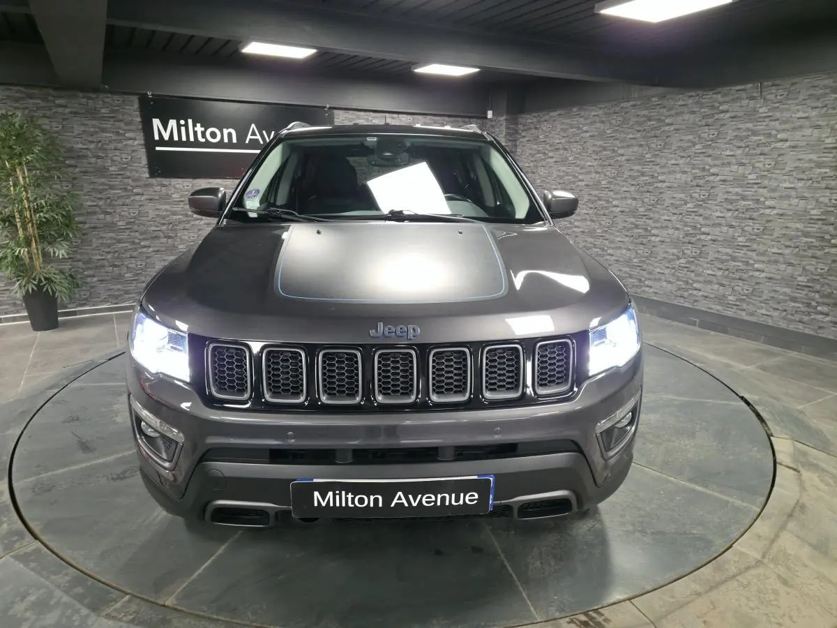 Vue de face du Jeep Compass gris métallisé avec calandre distinctive et phares allumés dans un showroom.