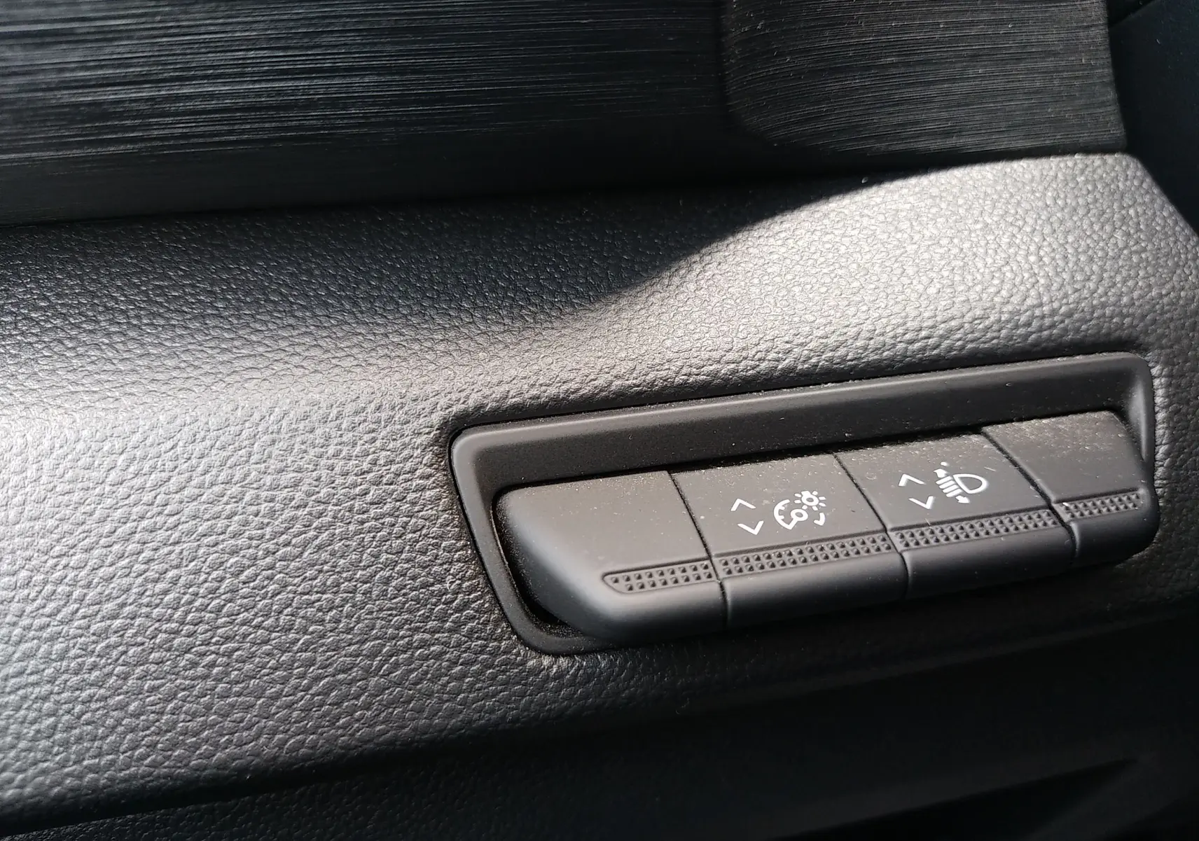 Gros plan sur les commandes de réglage des phares et de la luminosité sur la planche de bord noire du Renault Trafic Fourgon blanc.