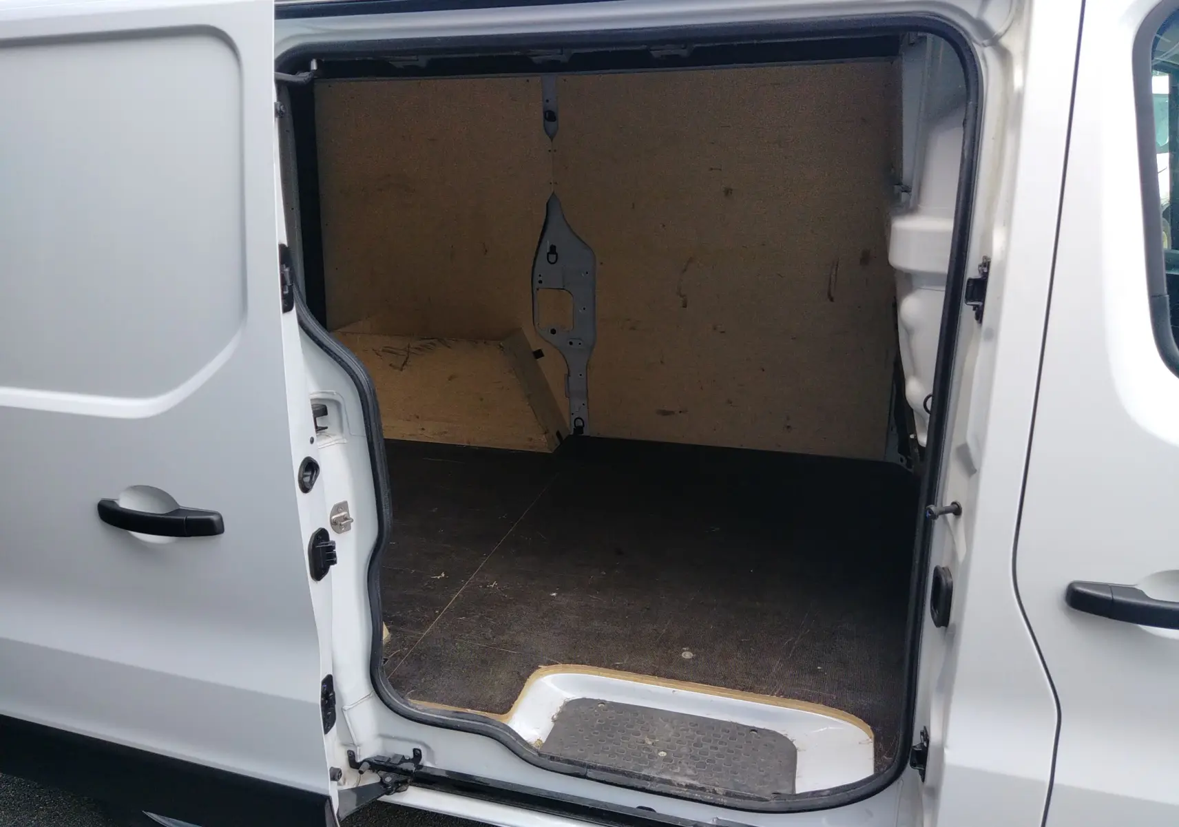 Vue intérieure du fourgon blanc Renault Trafic avec porte latérale ouverte, montrant l'espace de chargement vide.