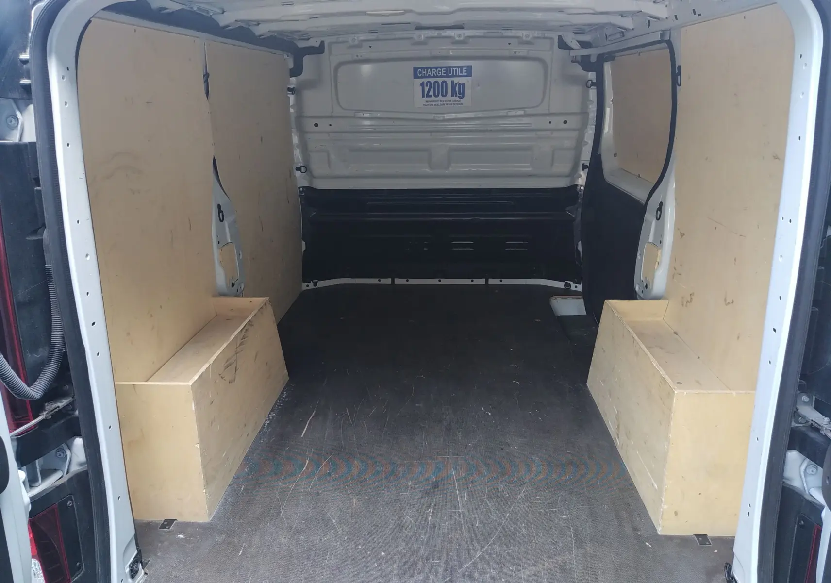 Vue intérieure arrière du Renault Trafic Fourgon blanc 2024, montrant l'espace de chargement avec panneaux bois et capacité 1200 kg.