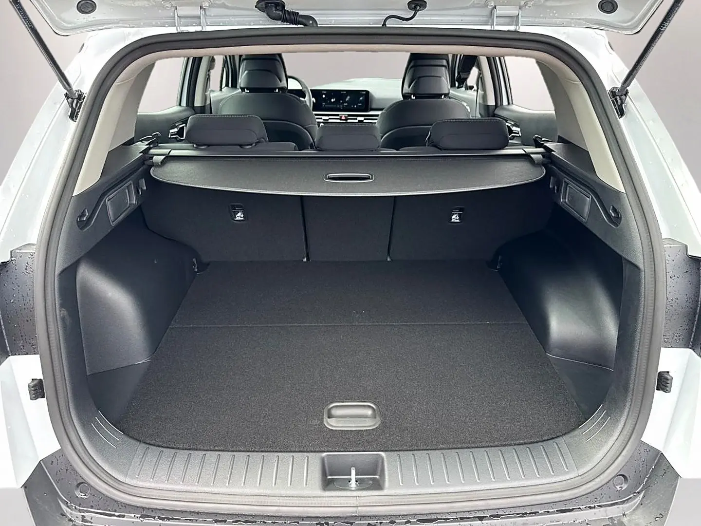 Coffre ouvert vu de l'arrière d'un KIA Sportage blanc 2026, avec cache-bagages et banquette arrière noire.