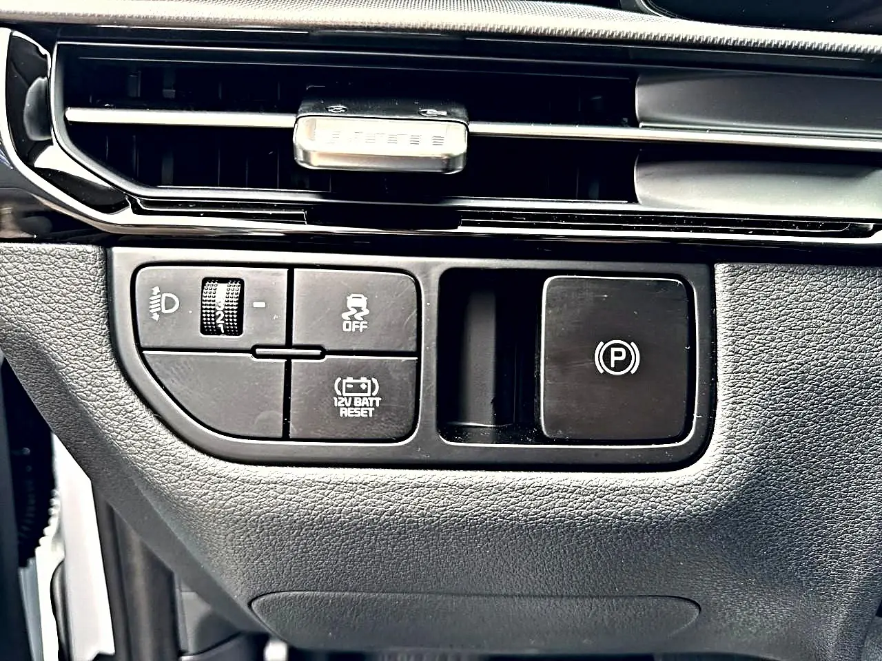 Gros plan sur les commandes noires du tableau de bord du Kia Sportage 1.6 hybride blanc, avec bouton frein à main électronique.