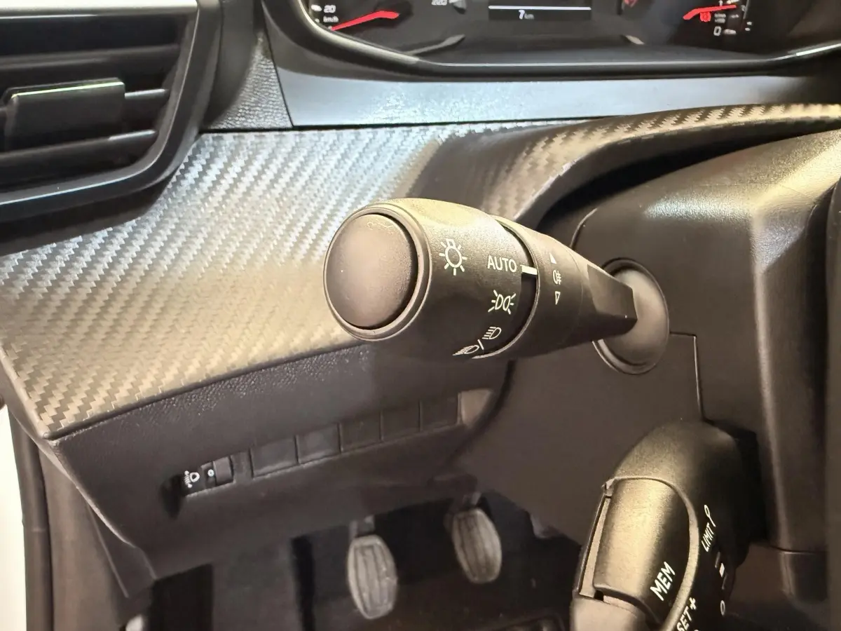 Gros plan sur la commande des phares et du régulateur de vitesse dans l'habitacle noir d'une Peugeot 208 blanche.