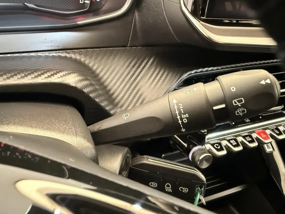 Gros plan sur la commande d’essuie-glace et tableau de bord carbone de la Peugeot 208 blanche, version 2025.