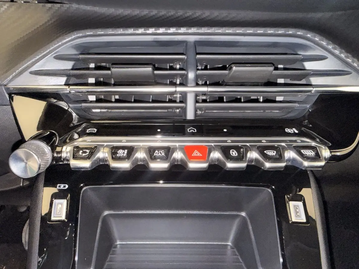 Gros plan sur la console centrale noire de la Peugeot 208 blanche, avec boutons de commande et prises USB visibles.