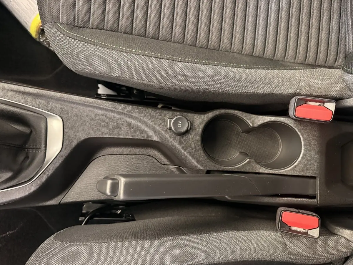 Vue plongeante sur la console centrale noire de la Peugeot 208 blanche, avec frein à main, prise 12V et porte-gobelets.