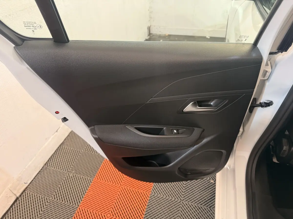 Vue intérieure de la porte arrière droite noire d'une Peugeot 208 blanche 2025, avec poignée et commande de vitre.