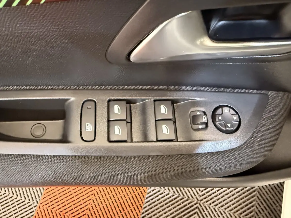 Gros plan sur la commande des vitres et rétroviseurs côté conducteur d'une Peugeot 208 blanche, intérieur noir.