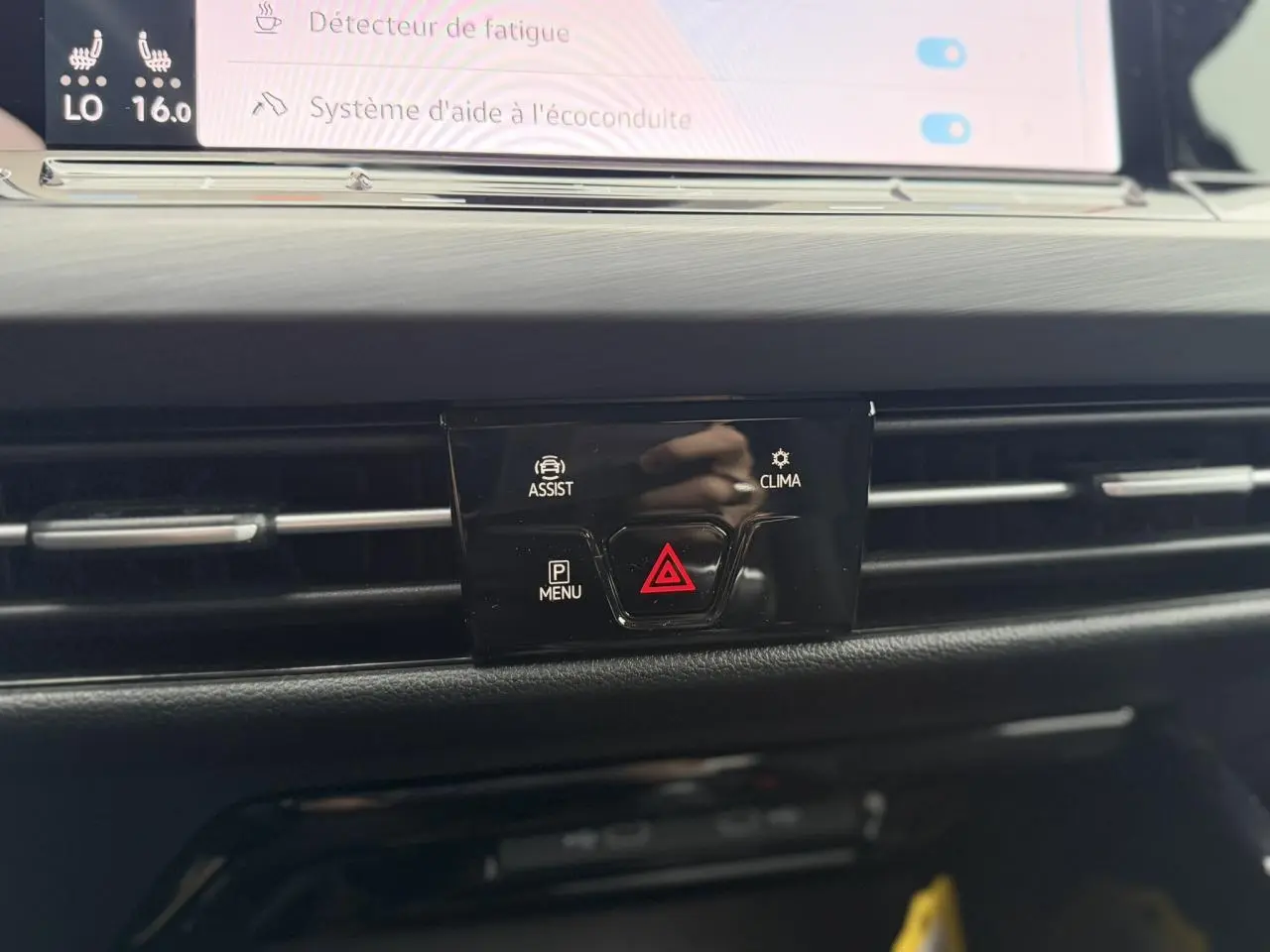 Gros plan sur la console centrale noire avec boutons d'alerte et d'assistance de la Volkswagen Golf VIII blanche.
