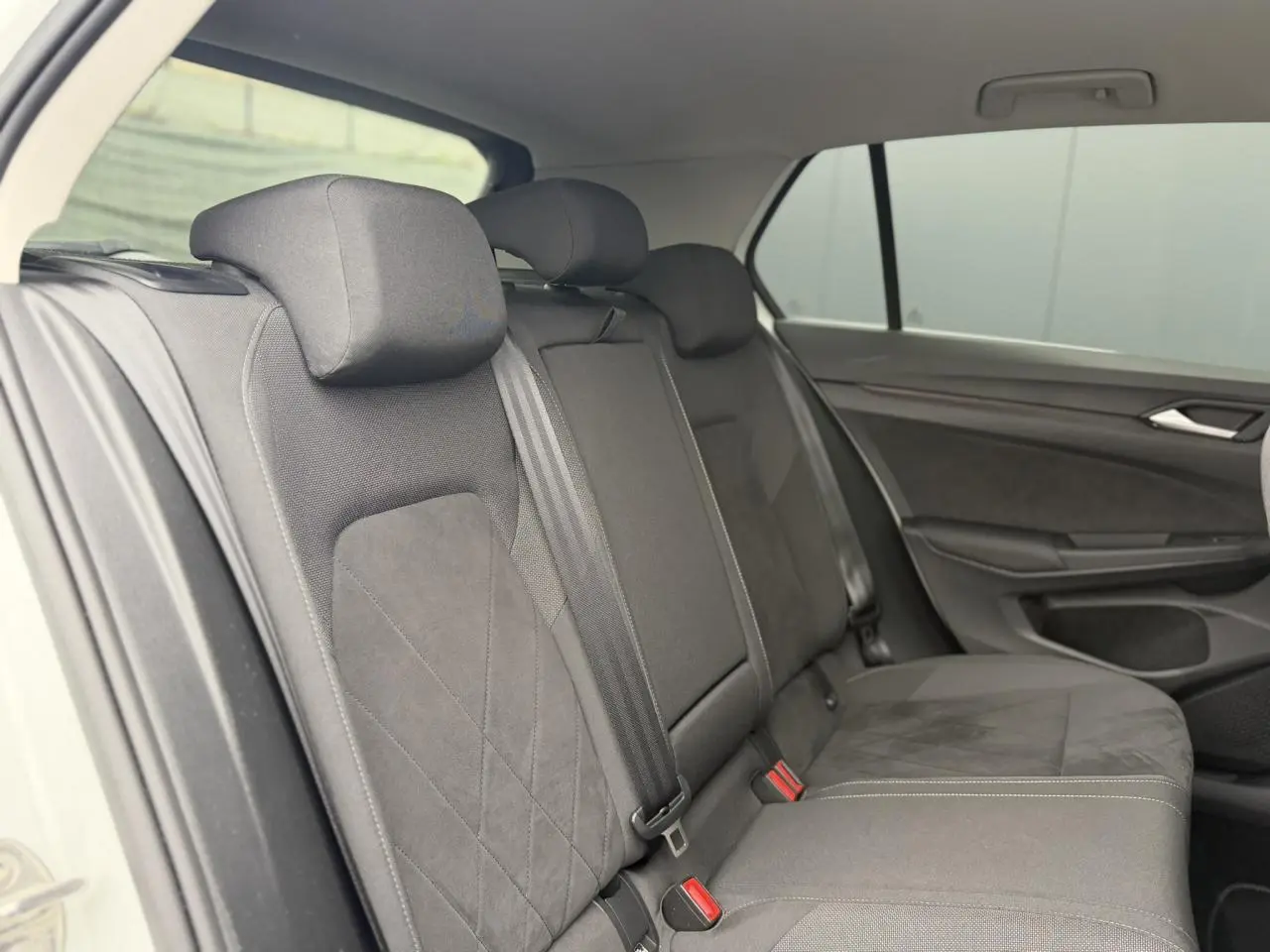 Vue intérieure côté arrière droit montrant les sièges arrière en tissu microfleece gris foncé de la Volkswagen Golf VIII blanche.