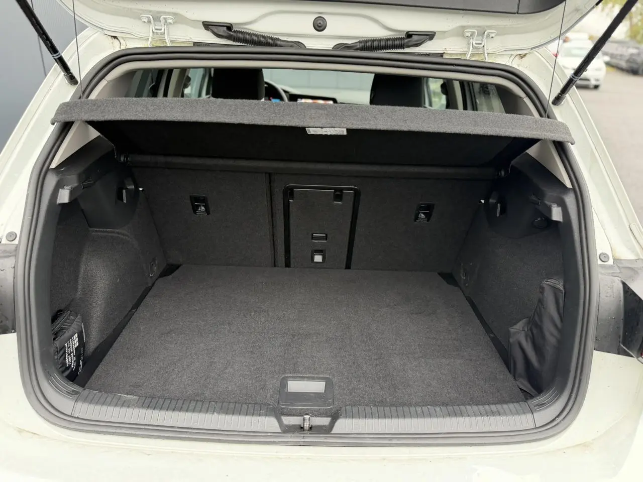 Coffre ouvert vu de l'arrière d'une Volkswagen Golf VIII 1.5 TSI blanche, montrant l'espace de chargement vide et la tablette arrière.