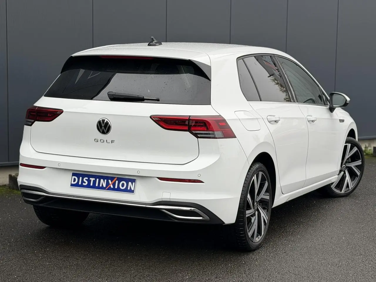 Vue 3/4 arrière droite d'une Volkswagen Golf VIII blanche avec jantes alliage 18 pouces et vitres arrière surteintées.