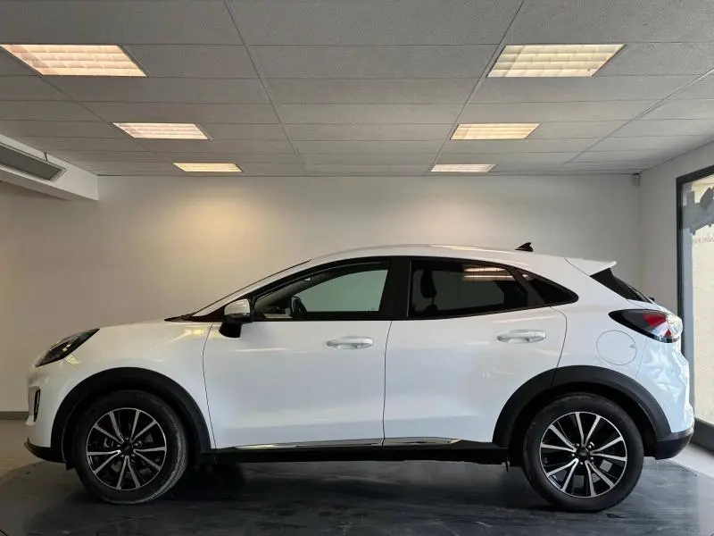 Ford Puma blanc glacier vu de profil côté gauche avec jantes noires et vitres arrière surteintées dans un showroom.
