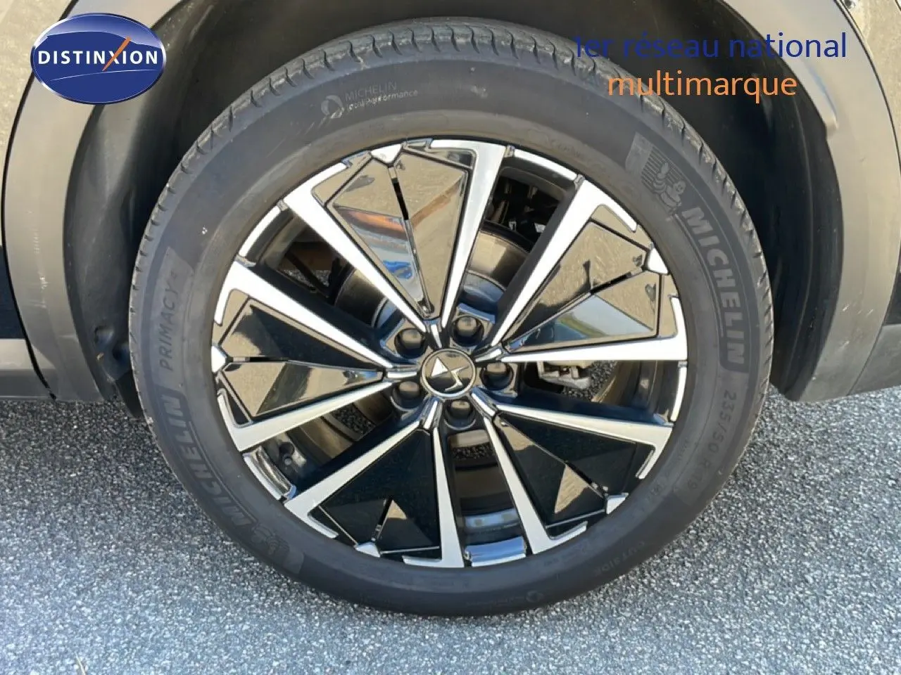 Gros plan sur la jante noire et argentée d’un DS7 2024 noir métal avec pneu Michelin sur sol goudronné.