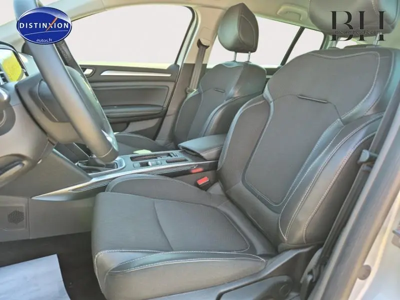 Vue intérieure côté conducteur de la Renault Mégane Break 2024 avec sièges tissu gris foncé et accoudoir central.