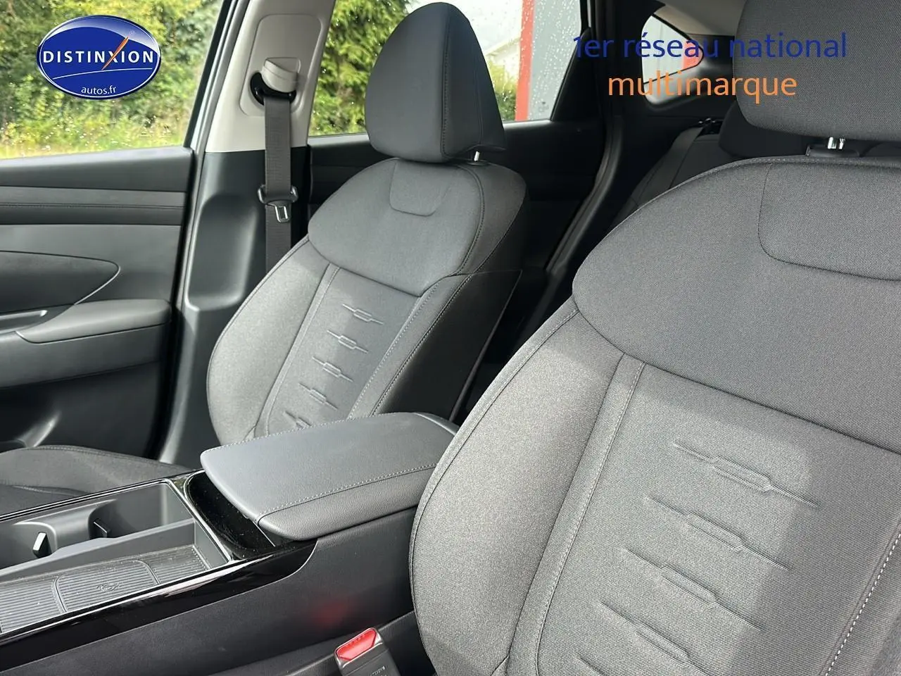 Gros plan sur les sièges avant gris du Hyundai Tucson 2025, mettant en valeur l'accoudoir central et la ceinture de sécurité côté gauche.