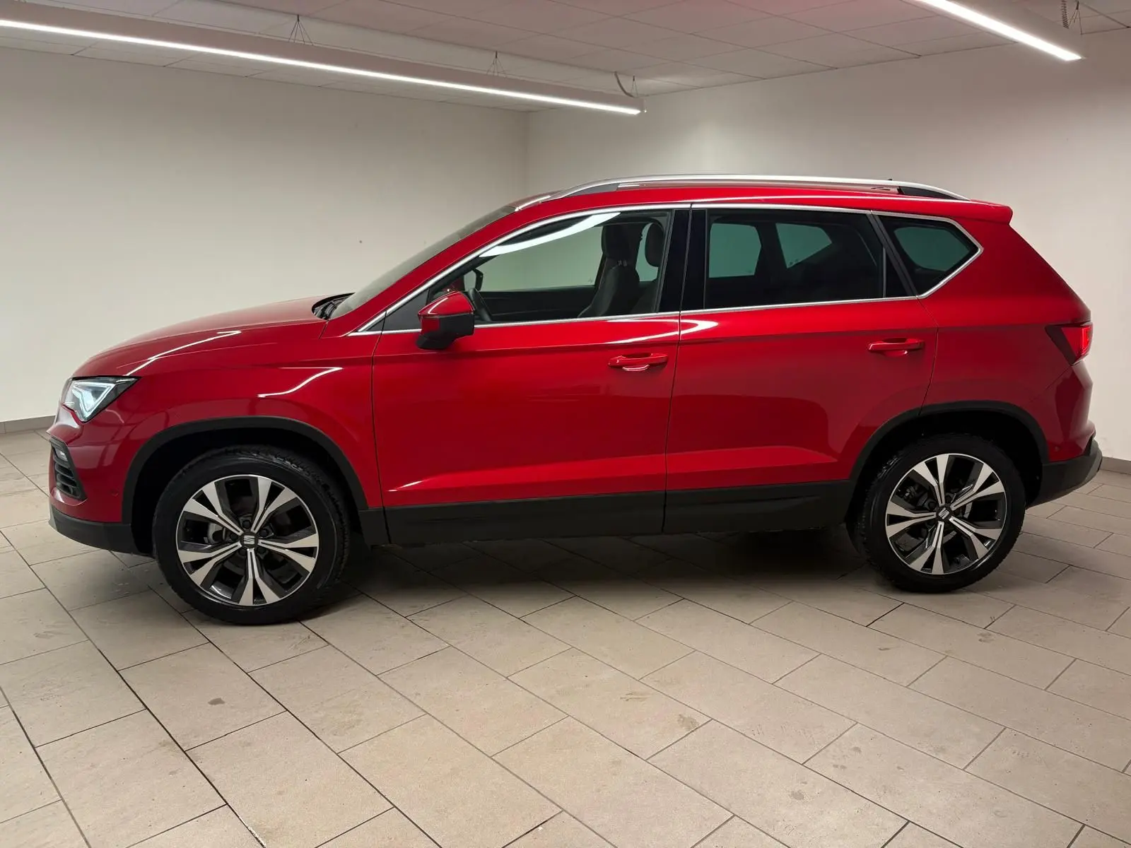 Vue de profil côté gauche d'un SEAT Ateca 2024 Rouge Velvet avec jantes alliage et toit ouvrant panoramique.