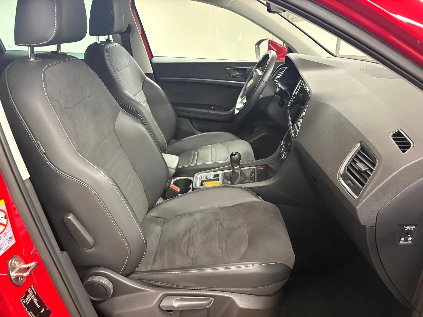 Vue intérieure côté conducteur du SEAT Ateca 2024 Rouge Velvet, avec sièges en cuir et alcantara, volant et levier de vitesses manuelle visibles.