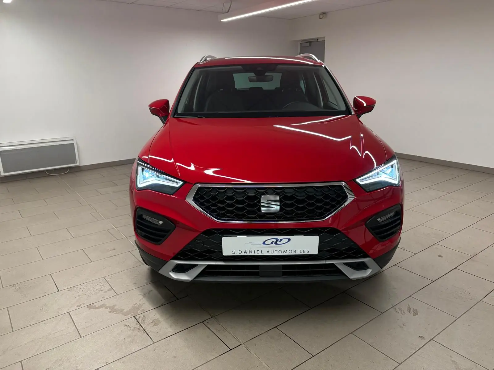 Vue de face du SEAT Ateca 2024 en Rouge Velvet métallisé avec phares allumés dans un intérieur neutre.