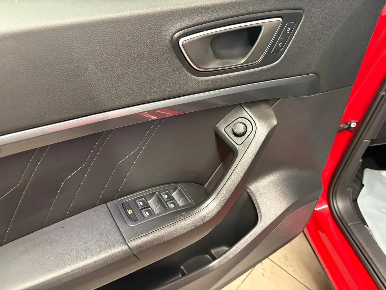 Gros plan sur la porte avant gauche rouge Velvet du SEAT Ateca 2024 avec commandes des vitres et réglage des rétroviseurs.