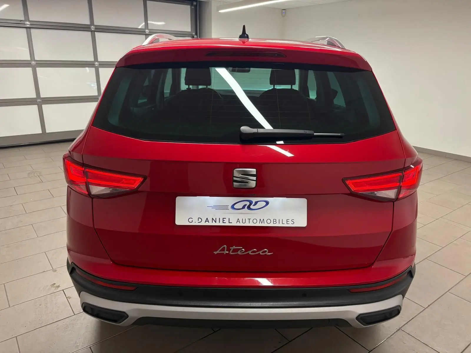Vue arrière d'un SEAT Ateca Rouge Velvet 2024, mettant en valeur les feux allumés et le logo central sur fond métallique.