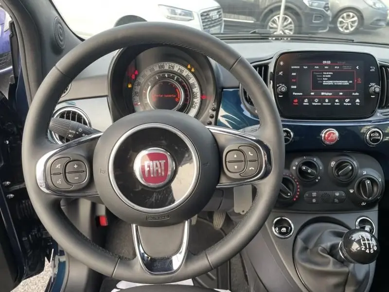 Vue intérieure centrée sur le volant FIAT d'une 500 bleu métal 2023 avec tableau de bord et levier de vitesse manuel.