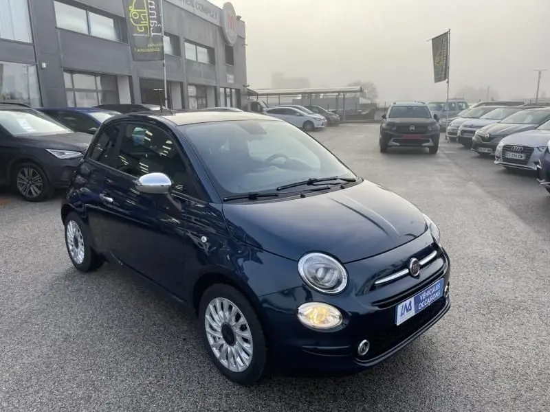 Fiat 500 bleu métal vue 3/4 avant droit, phare allumé, rétroviseurs chromés, stationnée en extérieur.