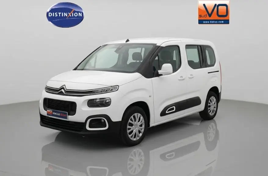 Citroën Berlingo blanc vue 3/4 avant droit avec protections latérales noires et barres de toit visibles.
