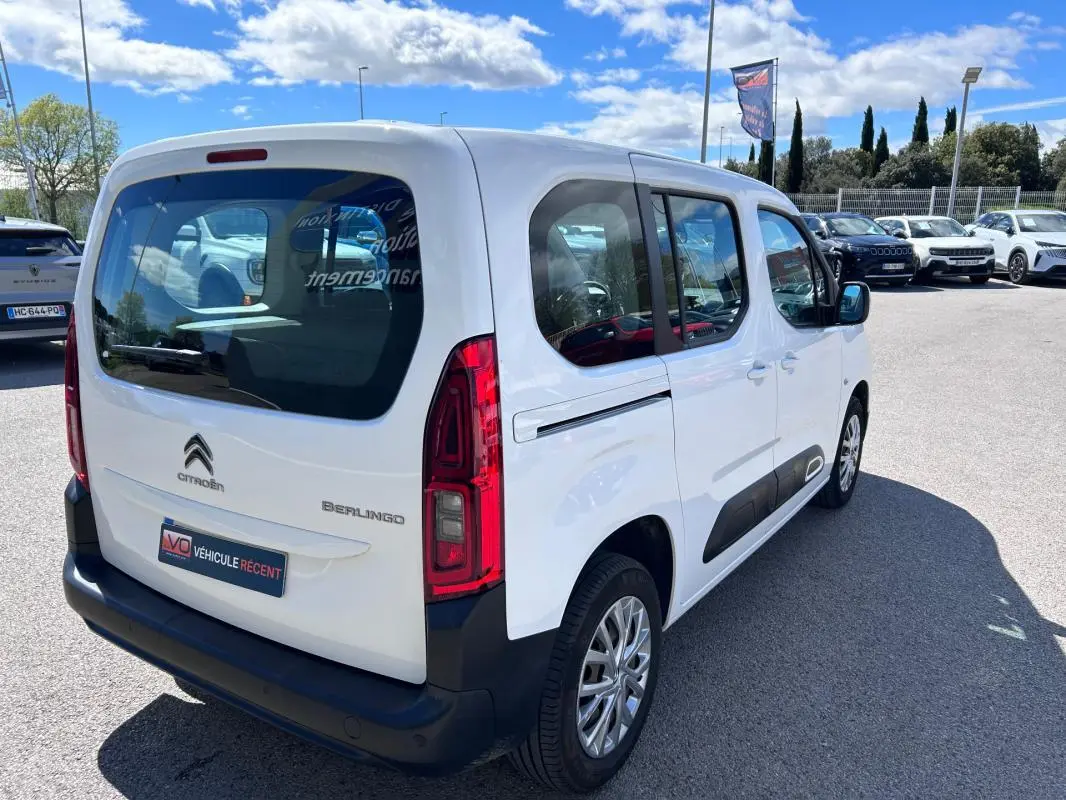 Vue 3/4 arrière droite du Citroën Berlingo blanc avec barres de toit et protections latérales noires.