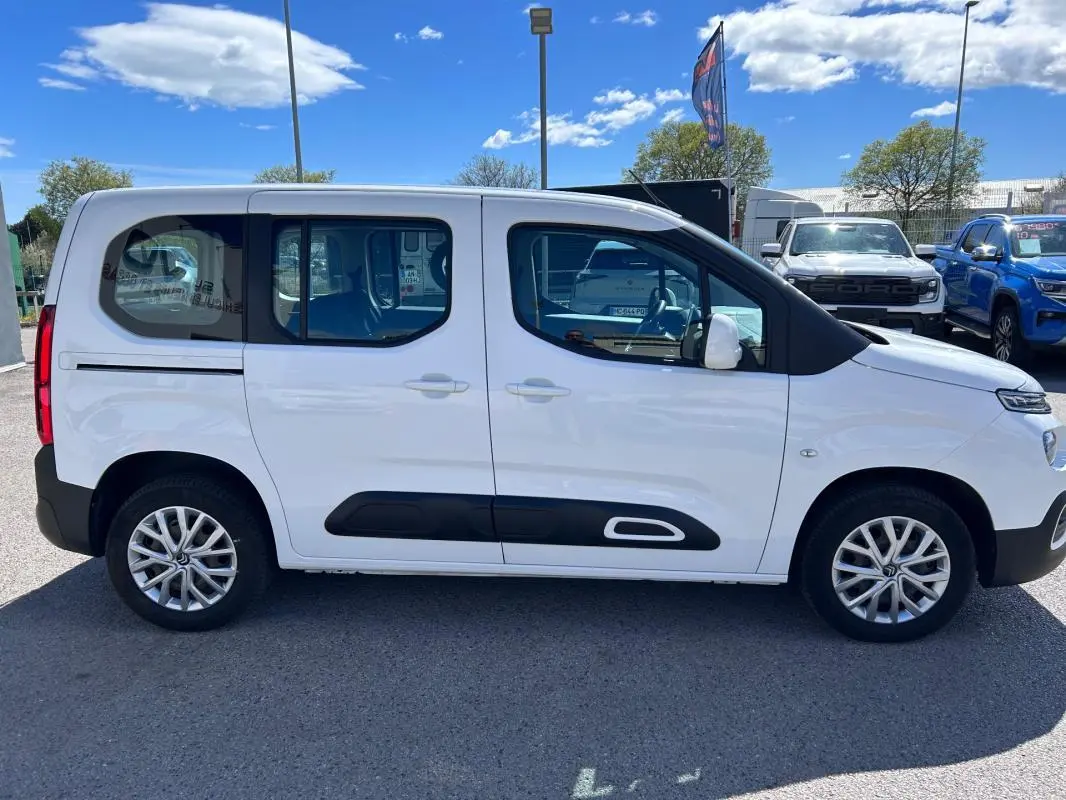 Profil côté droit du Citroën Berlingo blanc 2020 avec barres de toit et protections latérales noires.