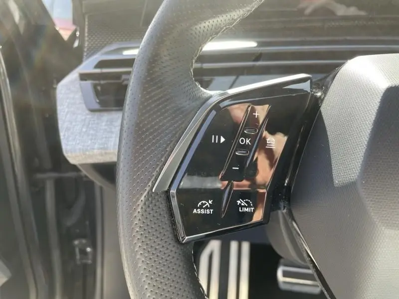 Gros plan sur les commandes gauche du volant perforé du Peugeot 3008 gris foncé 2024 hybride, avec boutons d'assistance et limiteur.