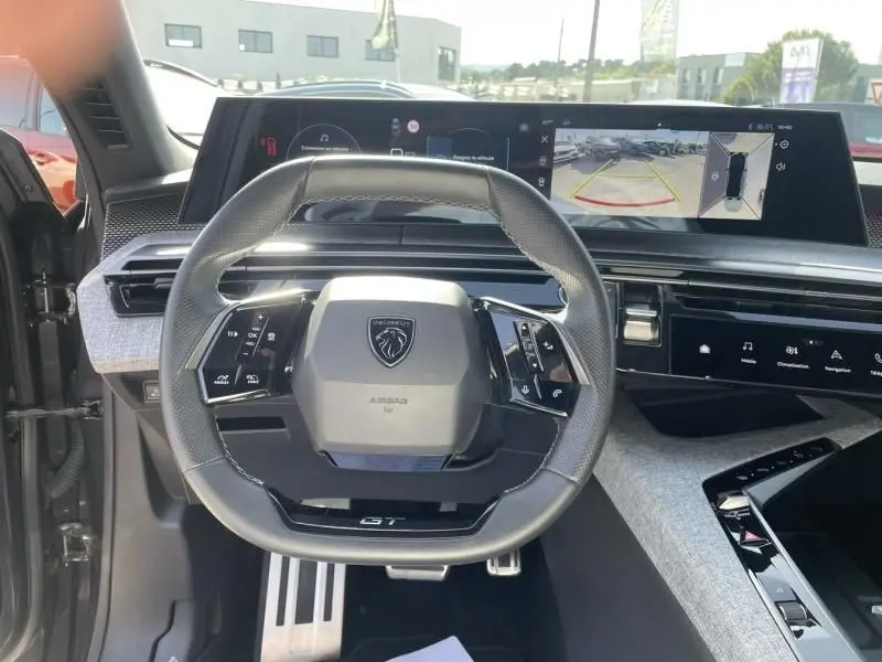 Vue intérieure centrée sur le volant GT du Peugeot 3008 2024 gris foncé avec tableau de bord numérique et caméra de recul.