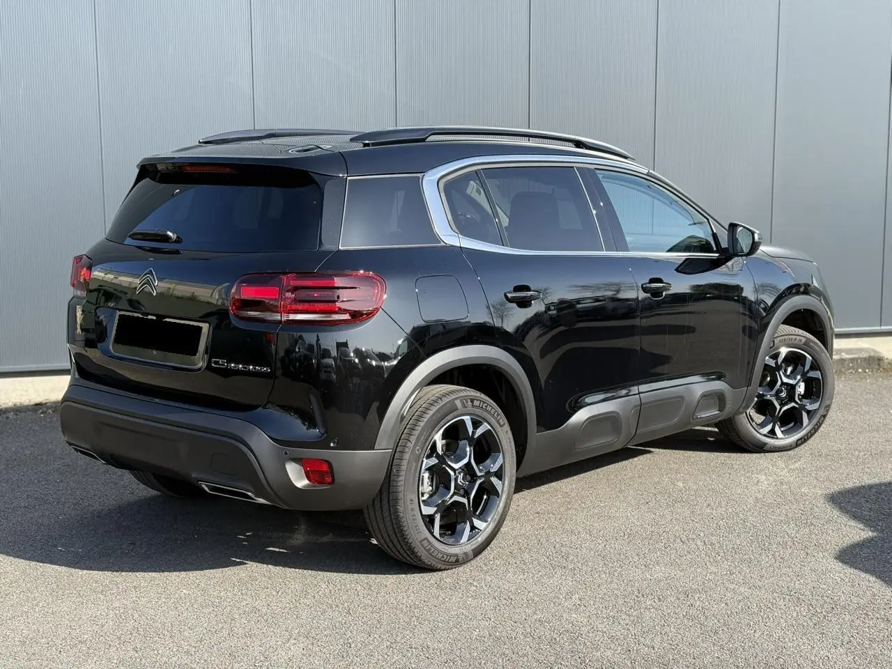 Vue 3/4 arrière droite du Citroën C5 Aircross noir Perla avec jantes alliage 18'' bi-ton et barres de toit noires.