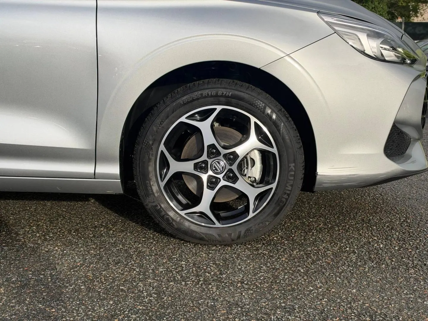 Gros plan sur la roue avant gauche et la partie avant d'une MG3 Cosmic Silver métallisé, avec jante alu distinctive.