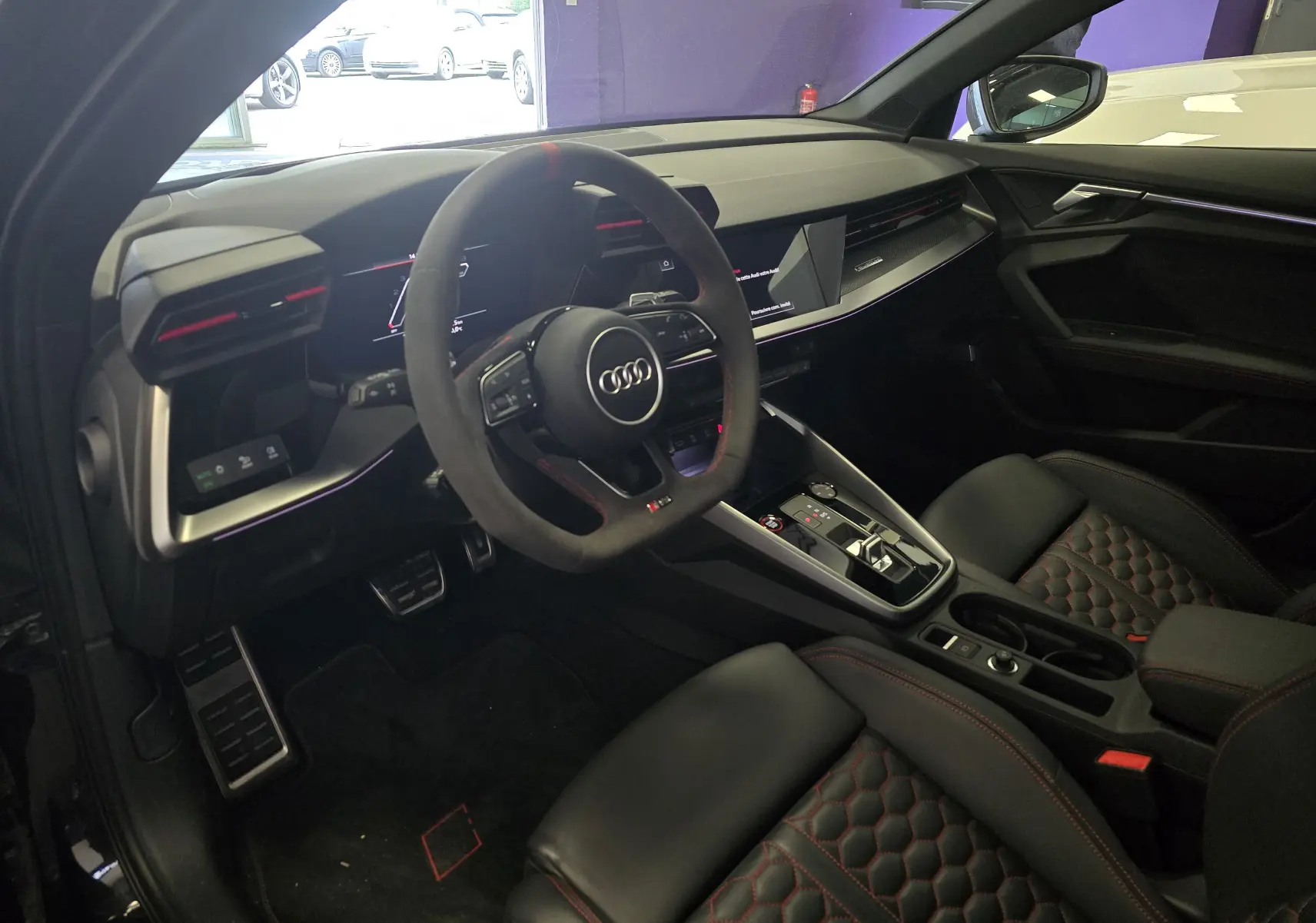Intérieur noir de l'Audi RS3 Sportback 2023, vue côté conducteur, volant sport, sièges cuir avec surpiqûres rouges.