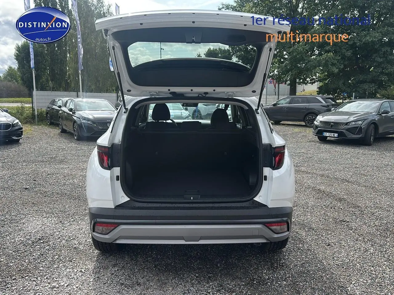 Vue arrière d'un Hyundai Tucson blanc sérénité 2025 avec coffre ouvert sur un parking extérieur.