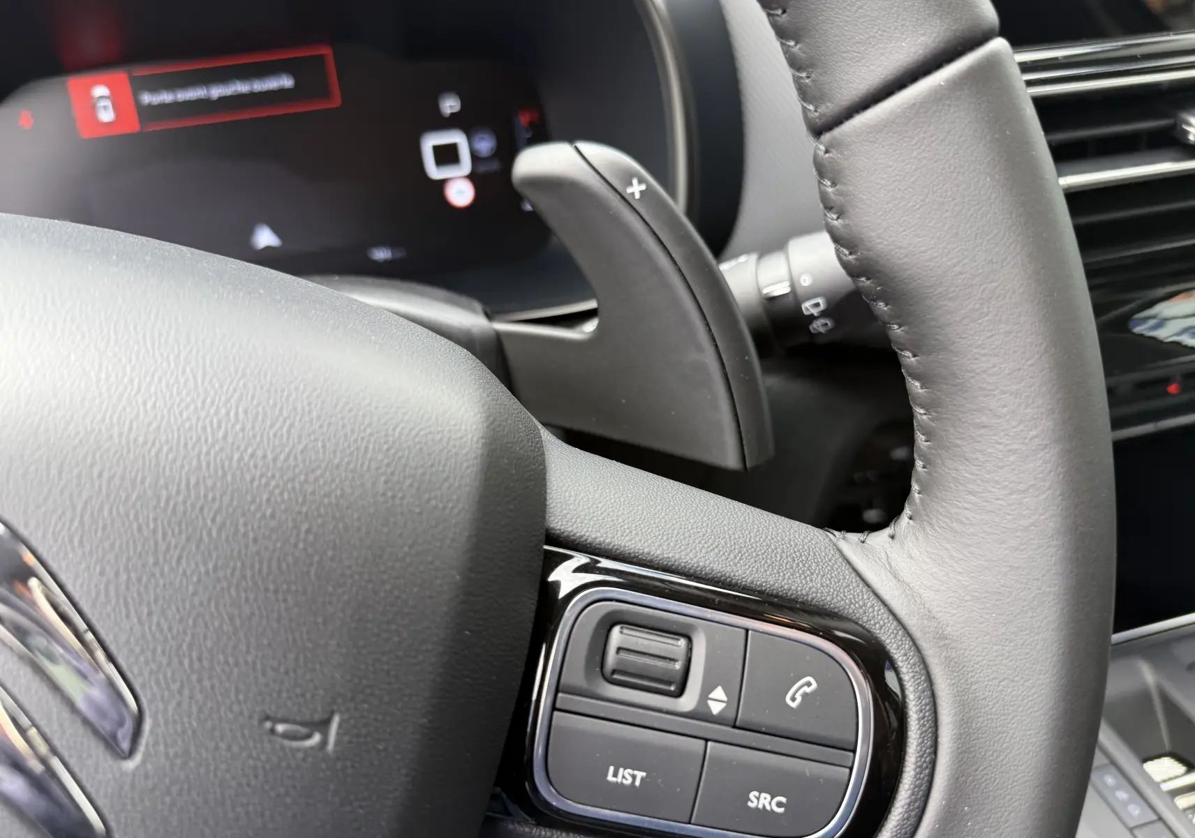 Gros plan sur le volant en cuir noir et la commande multifonction du Citroën C5 Aircross 2025, tableau de bord numérique en arrière-plan.
