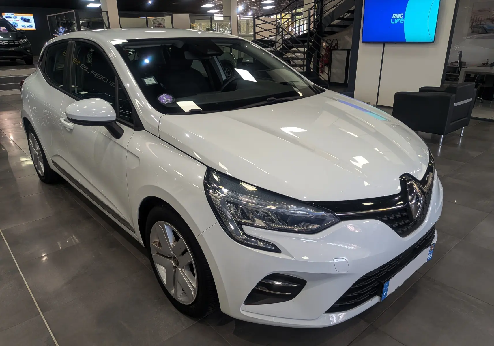 Renault Clio V TCe 100 Business blanc glacier vue 3/4 avant droit en showroom avec jantes spécifiques.