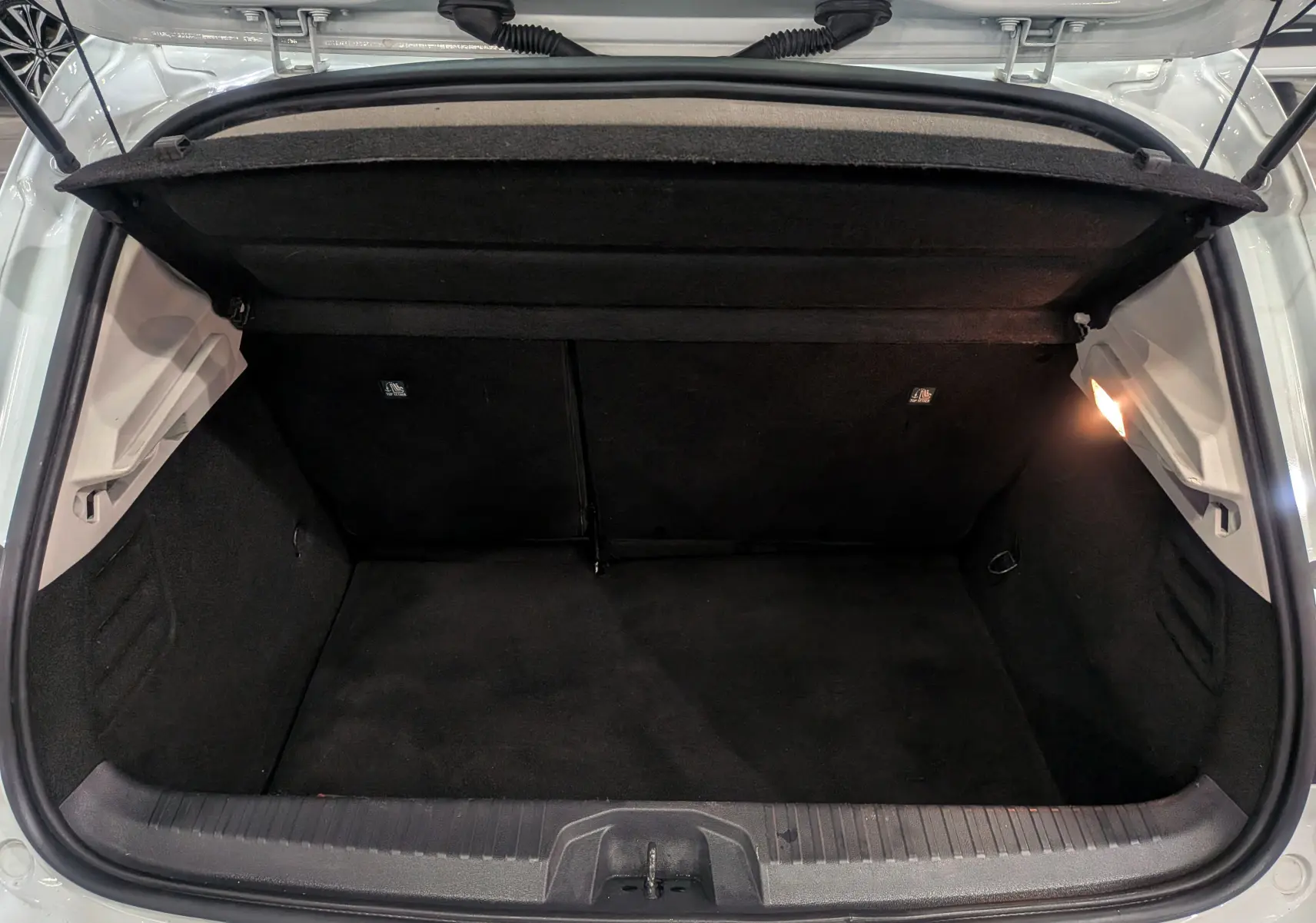 Coffre ouvert de la Renault Clio V TCe 100 Business blanc glacier, vue arrière montrant l'espace de chargement noir.