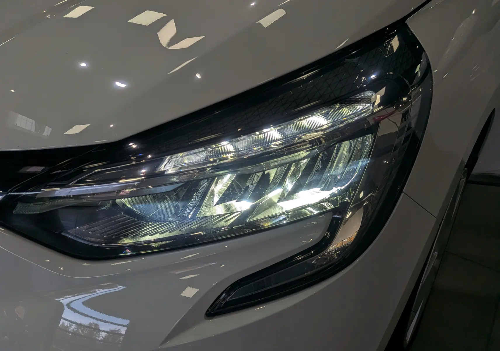 Gros plan sur le phare avant droit blanc glacier d'une Renault Clio V TCe 100 CH BUSINESS 2020, éclairage LED visible.