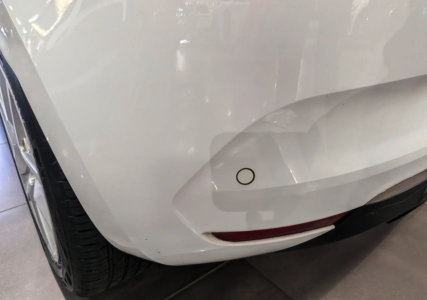 Gros plan sur le pare-chocs arrière droit blanc glacier d'une Renault Clio V TCe 100 CH BUSINESS avec capteur de recul visible.