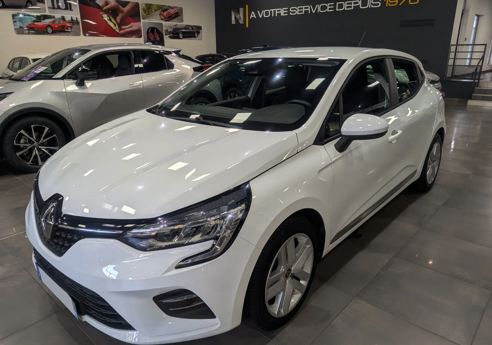 Renault Clio V TCe 100 Business blanc glacier vue 3/4 avant droit en showroom avec jantes alliage.