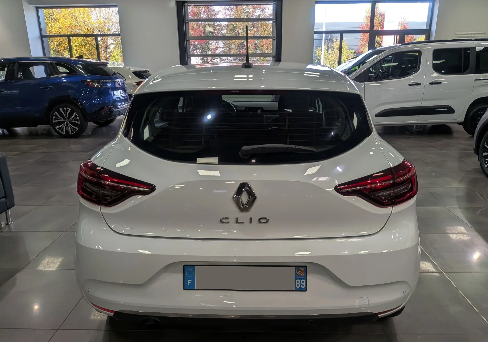 Vue arrière d'une Renault Clio V blanche Glacier, avec feux arrière LED et logo Renault bien visibles en intérieur showroom.