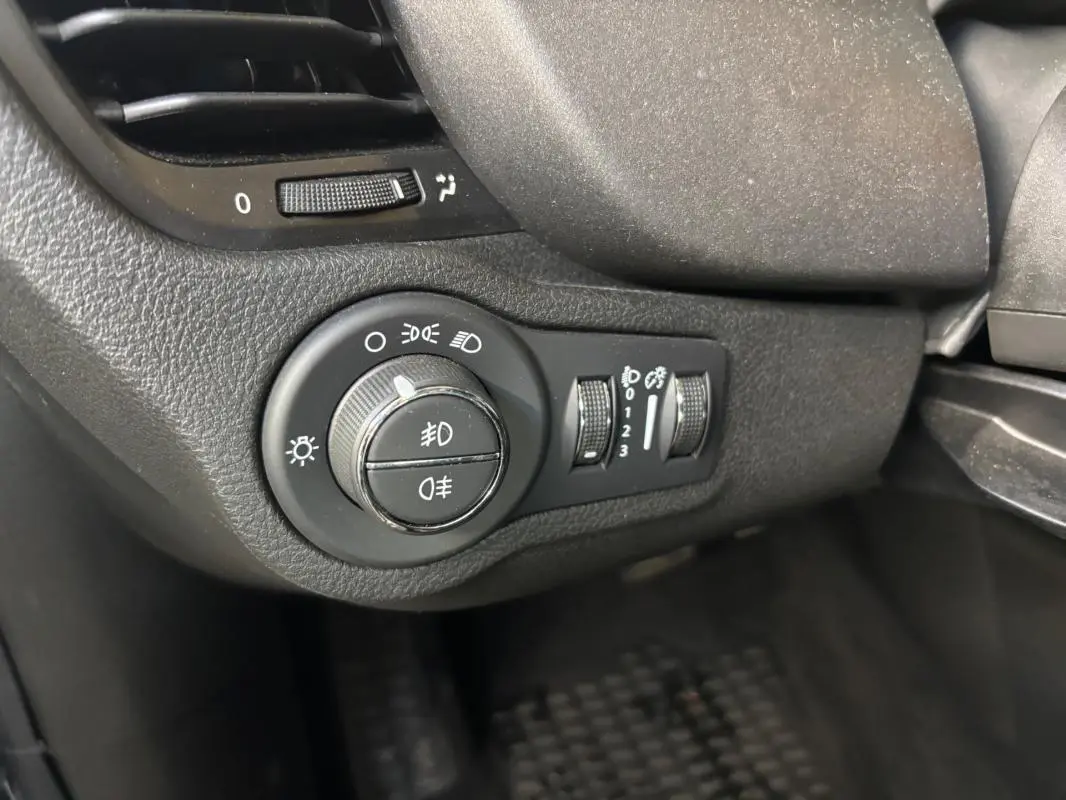 Gros plan sur la molette des phares et commandes d’éclairage du tableau de bord d’une FIAT 500X gris MY23.