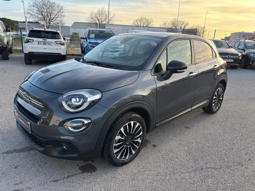 Vue 3/4 avant droit d'une FIAT 500X MY23 gris métallisé avec jantes classiques 16 pouces sur parking extérieur.