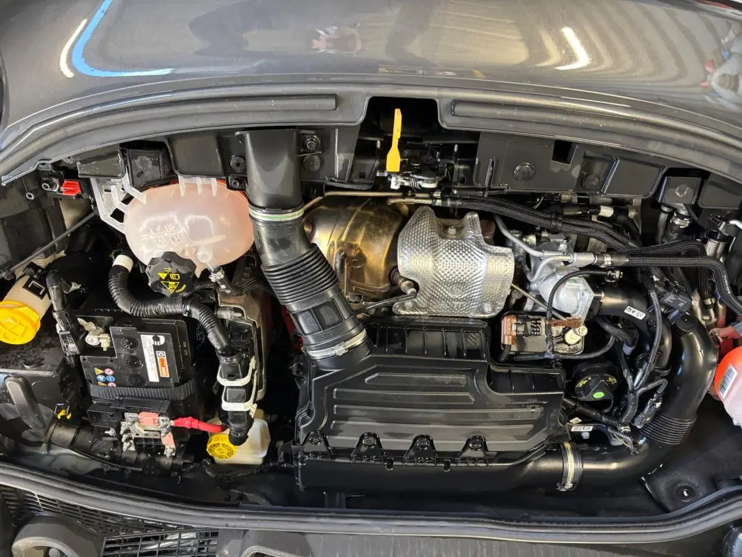 Vue plongeante sur le moteur gris d'une FIAT 500X MY23 1.5 FireFly hybride avec composants et durites visibles.