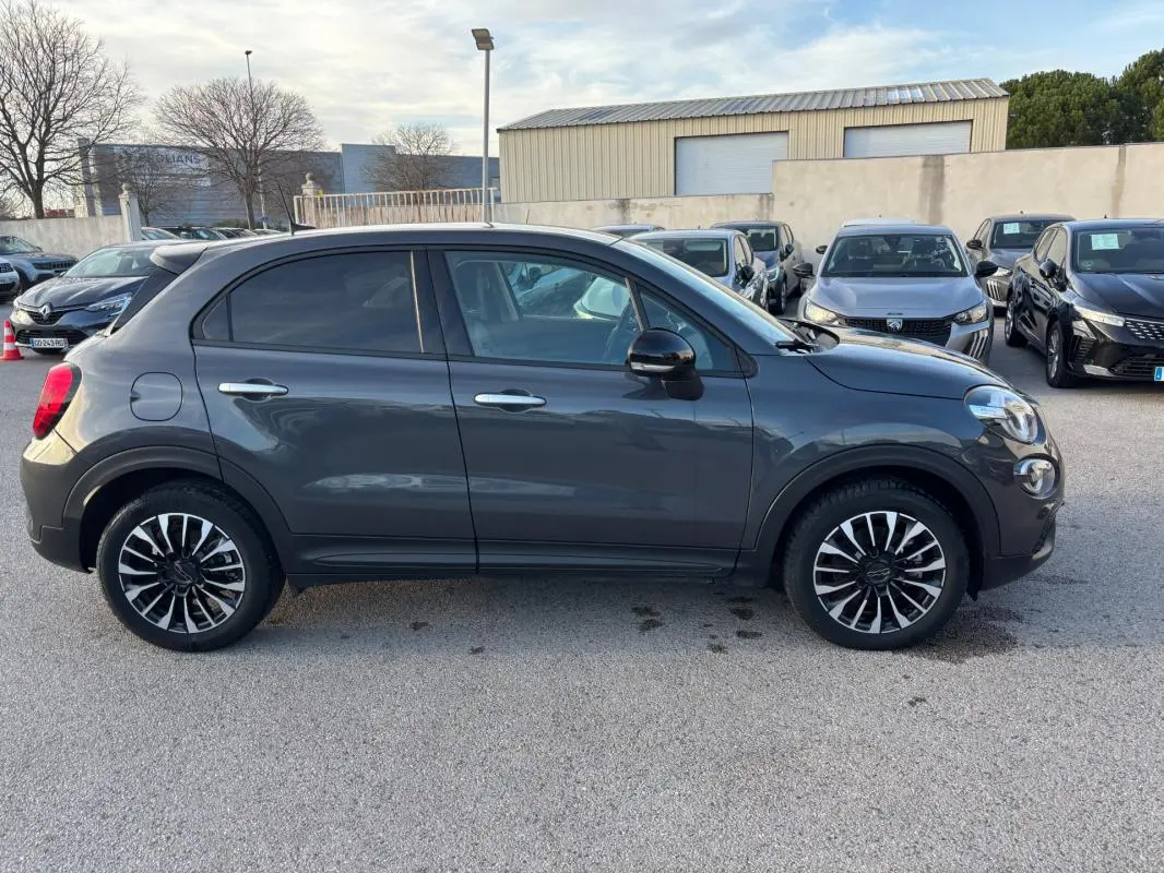 Profil droit d'un FIAT 500X gris 2023 avec jantes noires et argent classiques, stationné en extérieur.