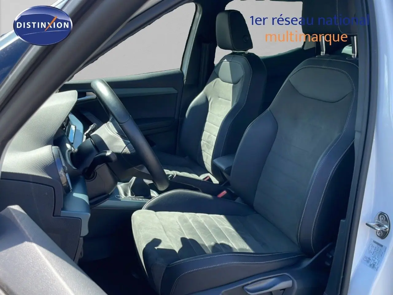 Vue intérieure côté conducteur du SEAT Arona 2025, sièges en tissu noir avec surpiqûres blanches, volant cuir multifonction.